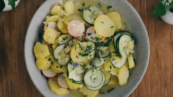 Kartoffelsalat mit Schale, garniert mit Radieschen, Gurken und Schnittlauch. Ein herzhaftes Gericht, das an Omas Küche erinnert.