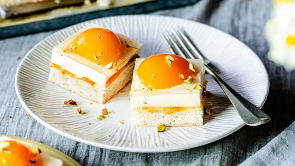 Zwei exquisite Stücke spiegeleikuchen mit pudding, garniert mit Pfirsich und Pistazien, auf einem Teller mit einer Gabel.